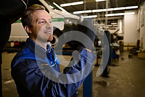 Auto mechanic picks up a nut while servicing a car in a car workshop. Car maintenance and auto service concept