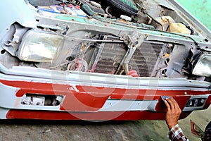 Auto mechanic preparing the front bumper of a car for painting