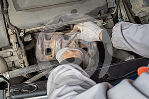 An auto mechanic removes the exhaust manifold to collect and remove exhaust gases from the cylinders of a passenger car engine