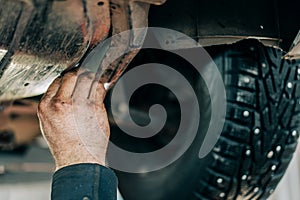 An auto mechanic removes the undershield of an internal combustion engine on a car. Scheduled maintenance and oil change