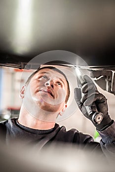 Auto mechanic repairer checking condition under car on vehicle lift