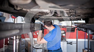 Auto mechanic repairer checking condition under car on vehicle lift