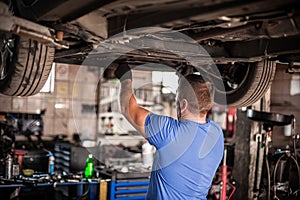 Auto mechanic repairer checking condition under car on vehicle lift