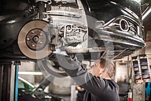 Auto mechanic repairer checking condition under car on vehicle lift