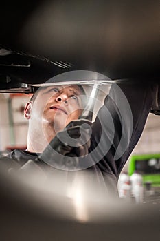 Auto mechanic repairer checking condition under car on vehicle lift