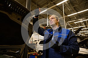 Auto mechanic repairer checking level of oil in car engine, under the hood, of the vehicle service shop