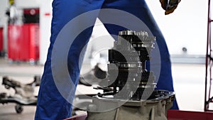 Auto mechanic repairs manual transmission in garage. Professional technician in blue uniform dismantles gearbox, fixes