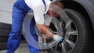 Auto mechanic secures car wheel with torque wrench for precision. Worker in uniform installs tire ensuring safety