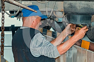 Auto mechanic stands in inspection pit of car service and repairs truck. Real locksmith fixes problems on truck.