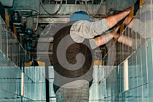 Auto mechanic stands in inspection pit of car service and repairs truck. Real locksmith fixes problems on truck.