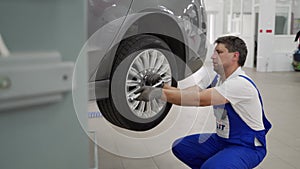 Auto mechanic in uniform installs alloy wheel on sedan using torque wrench at high-end service center. Skilled