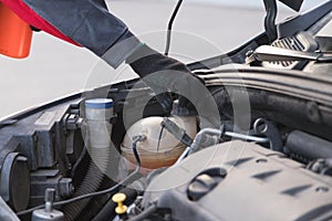 Auto mechanic unscrews expansion tank cap to pour antifreeze in car service workshop
