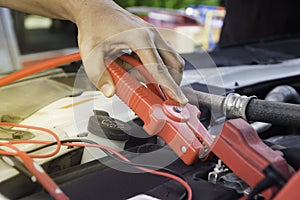 Auto mechanic uses a charging battery with electricity trough jumper cables in a car.
