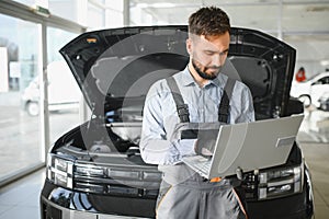 Auto mechanic using computer diagnostic program while repairing car in workshop