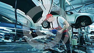 Auto mechanic using a lamp to check under the hood of a car