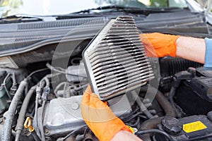 Auto mechanic wearing protective work gloves holding dirty air filter above a car engine