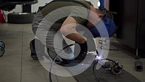 Auto mechanic welds exhaust pipe in workshop. Welding sparks fly from flex pipe as repairman fixes vehicles exhaust