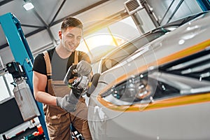 Auto mechanic worker polishing car at automobile repair and renew service station shop by power buffer machine