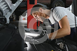 Auto mechanic working on car engine in mechanics garage. Repair service.