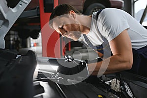 Auto mechanic working on car engine in mechanics garage. Repair service.