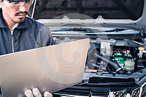 Auto mechanic working on a computer connected to a car engine at repair shop