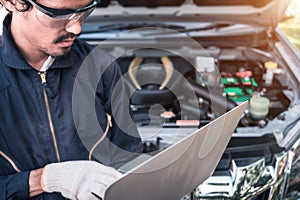 Auto mechanic working on a computer connected to a car engine at repair shop