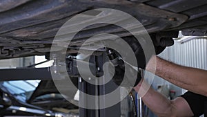 An auto mechanic working under a car on a car lift in a garage. Auto repair shop