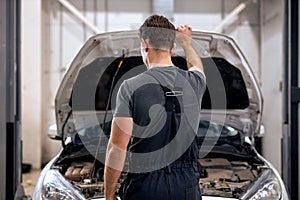 Auto mechanic working under car hood in repair garage, closing or opening the hood