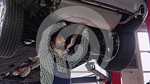 Auto mechanic working under car on hydraulic lift in garage
