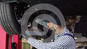 Auto mechanic working under car on hydraulic lift in garage