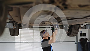 Auto mechanic working underneath car lifting machine at the garage. Auto repair shop. Male mechanic working on vehicle