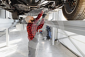 Auto mechanic working underneath a lifted car. Auto mechanic working in garage. Repair service