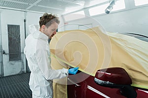 Auto painter covering car with paper before painting or polishing in spray booth.