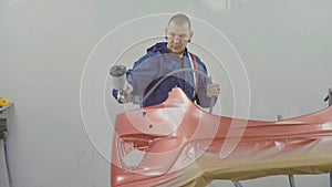 Auto painter spraying red paint on car front bumper in special booth