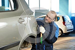 Automatické opravy muž pracovník vyrovnat a sladit kovové tělo auto s kladivem v automobilovém průmyslu.