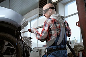 Auto repairman in protective glasses works spotter for car repair