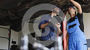 Auto Service. Car Service Employees Inspect the Bottom and Skid Plates of the Car. Manager Checks Data on a Notebook and