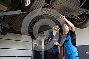 Auto Service. Car Service Employees Inspect the Bottom and Skid Plates of the Car. Manager Checks Data on a Notebook and