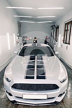 Auto service, car washing and cleaning concept. Handsome young Caucasian male worker in black t-shirt and cap, doing car