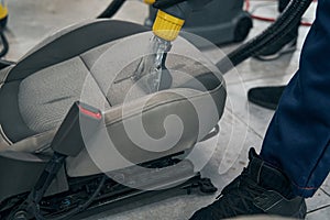 Auto service man washing removed front seat using vacuum cleaner