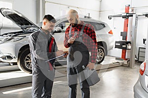 Auto service, repair, maintenance and people concept - mechanic men with wrench repairing car engine at workshop