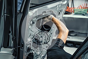 Auto service worker disassembles car door for repair, restoration, tuning car sound or installing noise insulation or