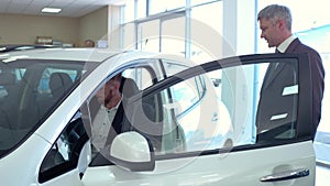 Auto showroom, sales manager showing new car to young man.