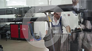 Auto technician mounts tire in modern workshop. Mechanic in uniform inspecting vehicle wheel, uses equipment, ensures