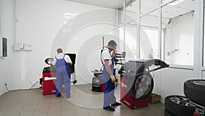 Auto techs work in tire shop, servicing vehicle wheels with changer, balancer tools. Uniformed workers remove, replace