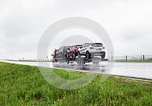 An auto transporter with a trailer transports cars in cloudy rainy weather on a slippery highway. Car carrier services