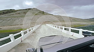 Auto travel: SUV rides on a high mountain road on white bridge over a river. POV - Point of view of a car moving on the