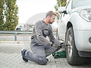 The mechanic changes the wheel of the machine outdoors.