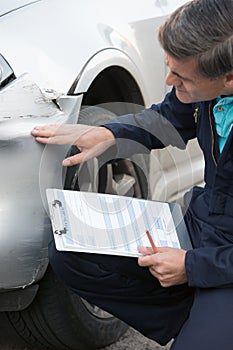 Auto Workshop Mechanic Inspecting Damage To Car And Filling In R