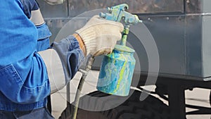 Automalyar paints large equipment from a spray gun. A worker wearing works outside on a summer day